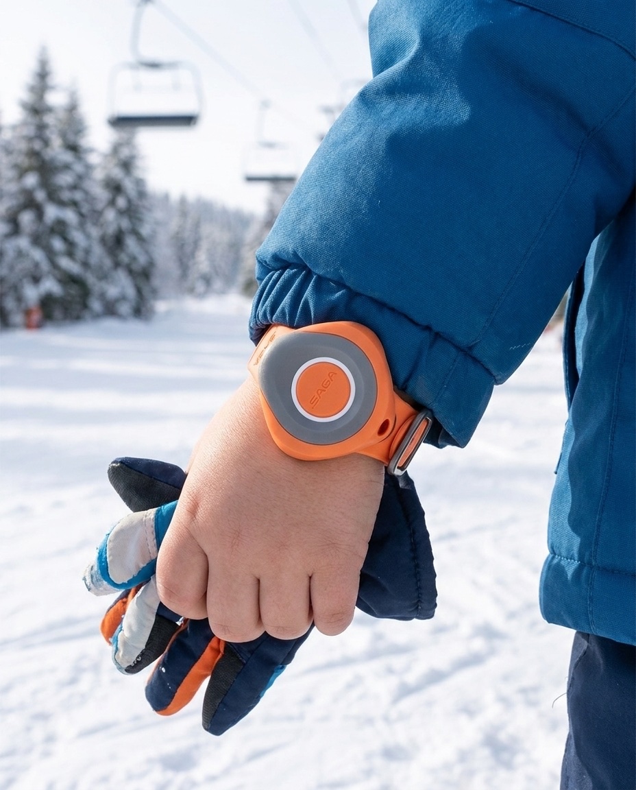 A young child in a blue ski jacket wearing an orange dot SAGA MyBand tag on the wrist, chairlift and snowy slope behind